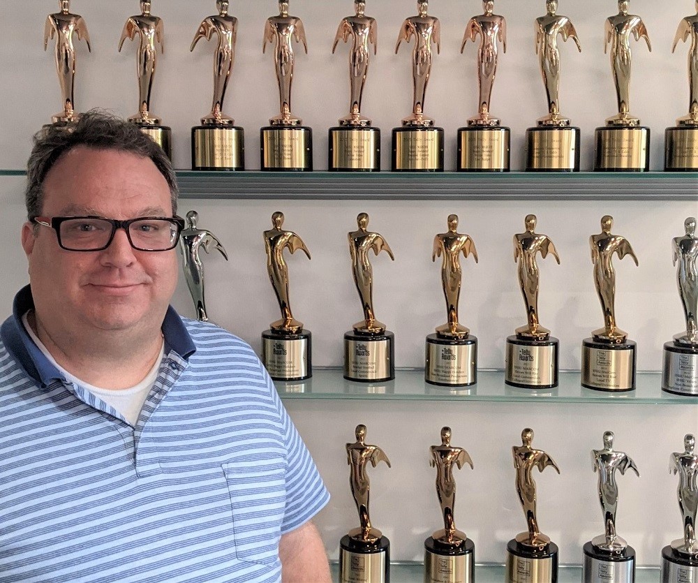 Mike Foster posing with the Telly Awards in the Marketing Office.